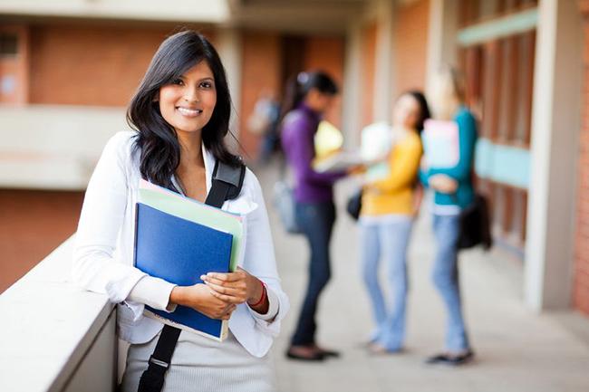 Woman holding books leaning against  wall