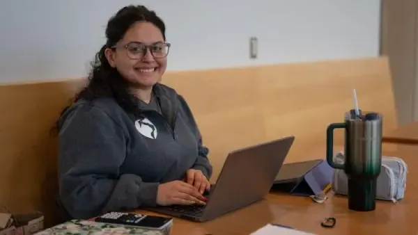 Female student working on her laptop smiling at the camera.